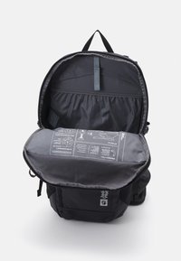 Black backpack with an open top, showcasing a grey interior and a printed instruction panel. Features include adjustable straps and a zipper closure.