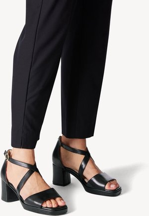 Czarne sandały na wysokim obcasie z kwadratowym noskiem, wykonane z gładkiej skóry. Posiadają skrzyżowane paski i masywny obcas.