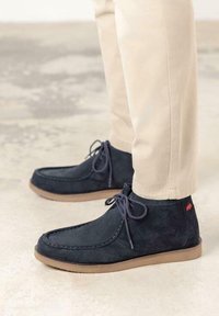 Botas de tobillo de ante azul marino oscuro con suela de goma marrón, que presentan detalles de costura y un acento del logo de conejo cerca del talón.