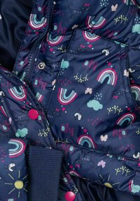 Chaqueta acolchada azul marino con patrones de gatos juguetones y arcoíris, con botones a presión rosas y puños elásticos, hecha de material resistente al agua.