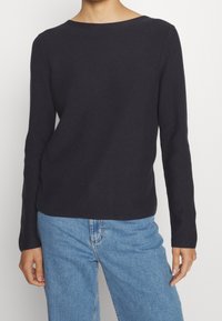 Haut côtelé bleu marine à manches longues avec un col rond. Associé à un jean en denim bleu clair, mettant en valeur une coupe décontractée et une texture douce.