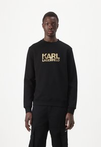 Sudadera negra con escote redondo, que presenta un gran texto en dorado "KARL LAGERFELD" en el pecho. Fabricada en tejido suave.
