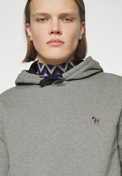 Hanorac gri cu șnur, având un logo colorat de zebră pe piept. Gulerul este suprapus cu o cămașă cu model.