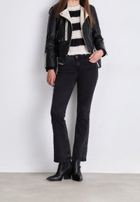 Chaqueta de cuero negra con cuello blanco, suéter de punto a rayas y jeans negros de talle alto acampanados. Botines negros completan el look.