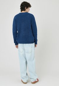 Pull en tricot bleu avec col rond, associé à un jean en denim léger bleu clair ample. Le tissu semble doux avec une finition texturée.
