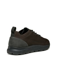 Scarpa sportiva nera con una parte superiore in maglia e un tallone di un grigio scuro liscio. Presenta una suola con un battistrada testurizzato e un'etichetta di sollevamento sul tallone.