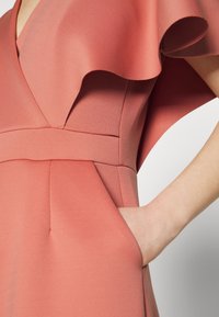 Ραφινάτη ροζ φόρεμα με βουβό λαιμό και πλευρική τσέπη. Απαλή ύφανση με σφιχτή μέση και ρο flowing μανίκια.