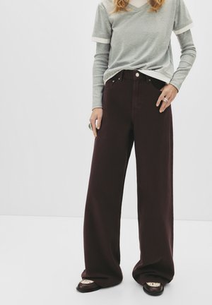 Weite, kastanienbraune Jeanshose mit hoher Taille, Fronttaschen und Knopfverschluss, kombiniert mit einem mehrlagigen grauen T-Shirt.