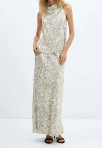 Lysefarvet maxikjole uden ærmer med paisley-mønster, draperet halsudskæring og flydende stof, kombineret med sorte sandaler med åben tå.