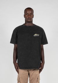Svart oversized t-skjorte i bomullsmateriale med rund hals, med en liten logo på venstre brystområde og en falmet tekstur.