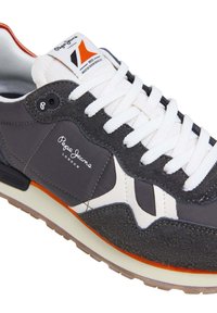Zapatilla deportiva gris con cordones blancos, parte superior de ante y cuero texturizado, acento naranja en la suela y detalle de logo en el lateral.
