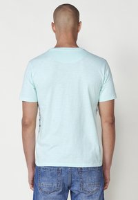 Ljusblå T-shirt med korta ärmar och rund halsringning. Mjuk, texturerad tyg; inga synliga mönster eller hårdvarudetaljer.