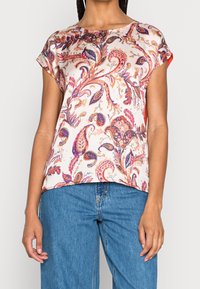 Kortærmet top i satin med blomster- og paisleymønster. Har rund halsudskæring og løs pasform med en cremefarvet baggrund og farverige detaljer.