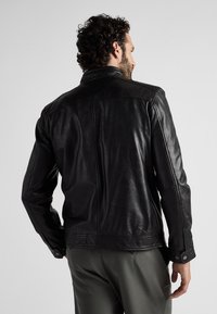 Zwarte leren jas met een gladde textuur, voorzien van een klassieke kraag, lange mouwen en knoopmanchetten. De achterkant toont een nette stiksel.