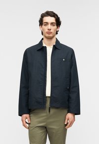 Μαύρο ελαφρύ μπουφάν με γιακά, εμπρός φερμουάρ και μία τσέπη στο στήθος. Λεία υφή, σχεδιασμένο με μινιμαλιστικό στυλ.