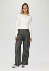Biała sweter ribbed z zamkiem na kołnierzu, zestawiony z ciemnymi spodniami o szerokim kroju w prążki i srebrnymi trampkami. Prosty, funkcjonalny design.