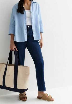 Jasnoniebieska koszula na guziki, biały top na ramiączkach, ciemnoniebieskie dżinsy, brązowe sandały z regulowanymi paskami oraz duża beżowa torba na ramię z czarnymi akcentami.