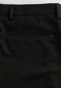 Pantaloni negri dintr-un material texturat, cu o croială slim, un model cu mici puncte și un singur buzunar la spate cu închidere ocultă cu buton.