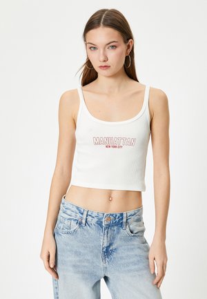 Valkoinen ribattu crop-top, jossa lukee punaisella "MANHATTAN NEW YORK CITY", yhdistettynä vaaleansinihin korkeavyötäröisiin farkkuihin, jotka tarjoavat rentoa istuvuutta.