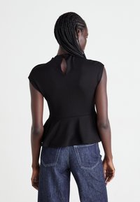Woman with braided hair wearing a sleeveless black peplum top and dark blue jeans, shown from the back against a white background.