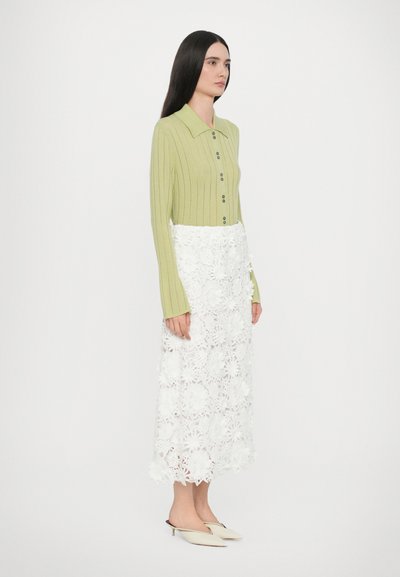 Grønn rippet strikket cardigan med krage, kombinert med en hvit midiskjørt i blomsterkant. Har lange ermer og knapplukking.