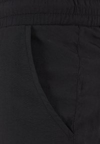 Tissu noir en gros plan montrant une poche latérale inclinée avec des coutures visibles sur une ceinture de vêtement.