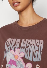 Sudadera gráfica marrón con el texto "SALT WATER", ilustraciones florales y de tabla de surf en rosa y blanco, con un cuello acanalado y una textura suave.