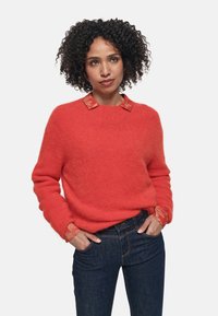 Maglione rosso in lana con finitura texturizzata, dotato di colletto e polsini a motivo contrastante, abbinato a jeans in denim scuri.