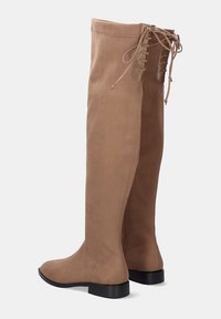 Botas de ante beige hasta la rodilla con punta redonda, cremallera lateral y detalle de cordones en la parte trasera; suela plana negra para mayor estabilidad.