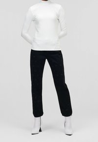 Biała bluzka z długim rękawem o fakturowanym wzorze diamentowym, zestawiona z czarnymi spodniami z delikatnymi akcentami i eleganckimi białymi botkami za kostkę.