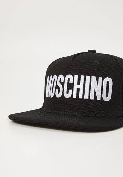 Casquette de baseball noire en tissu avec une visière plate et un logo "MOSCHINO" brodé blanc bien en évidence à l'avant. Détail de surface texturé.