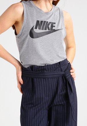 Kobieta ubrana w szary, bezrękawnikowy top Nike i granatowe spodnie w prążki z wysokim stanem oraz przewiązanym paskiem.