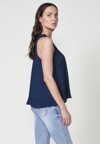 Top senza maniche di colore navy con orlo arricciato e dettagli in pizzo, realizzato in tessuto leggero. Abbinato a jeans blu chiaro.
