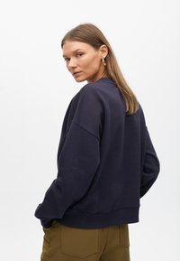 Sudadera de color azul marino con hombros caídos y bajo acanalado, combinada con pantalones de color verde oliva. Tejido suave y corte relajado.