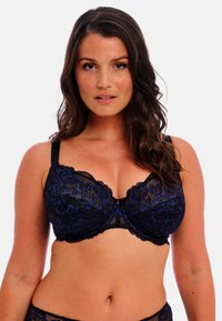 Černá krajková podprsenka s modrou květinovou výšivkou, s kosticemi, vlnitými okraji a nastavitelnými ramínky. Detail zapínání na háček uprostřed.