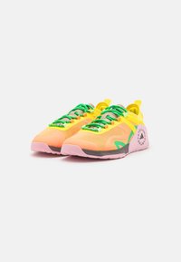Světlé žluté a růžové sportovní boty s zelenými tkaničkami, síťovaným materiálem, kulatou špičkou a výrazným logem na patě.
