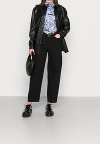 Chemise-jas de cuir synthétique noir sur un col roulé bleu marbré, associée à un pantalon large noir et des chaussures à lacets noires épaisses.