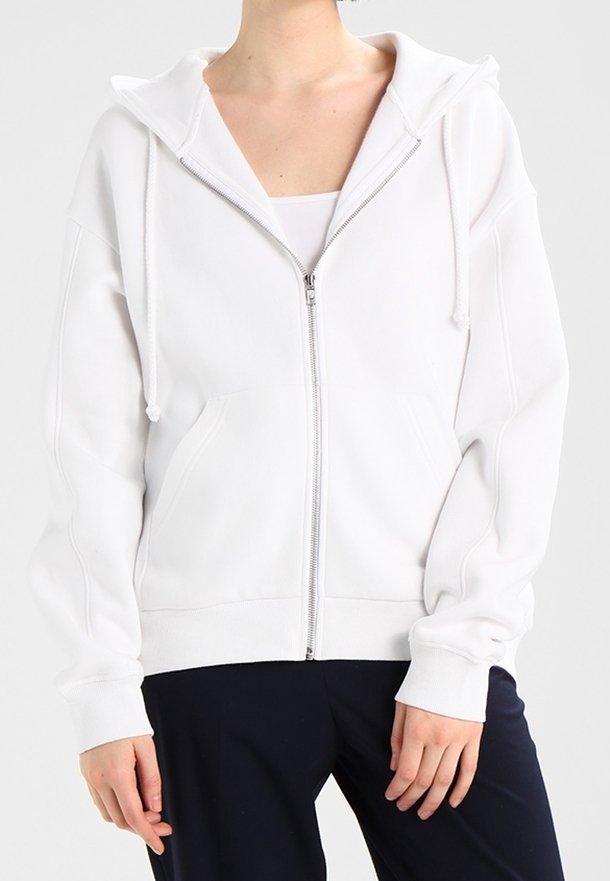 Sweat à capuche blanc zippé en matériau doux, doté d'une grande capuche, de cordons de serrage et de poches avant. Texture lisse et coupe décontractée.