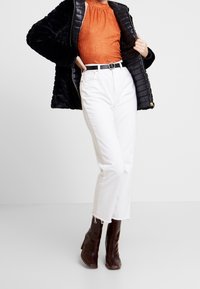 Svart puffjacka, orange mönstrad bodysuit, vita cropped jeans och bruna klackboots med ett strukturerat mönster samt ett runt svart bälte.