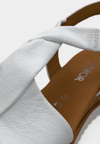 Άσπρο δερμάτινο σανδάλι με υφή στην επιφάνεια, διαθέτει φαρδιά λουράκια που διασταυρώνονται. Ταμπά εσωτερική σόλα με εμφανή λογότυπα.