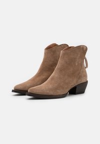 Botines de ante en color beige con punta afilada, tacón bajo y una lengüeta en la parte trasera. Textura suave y detalles de costura mínimos.