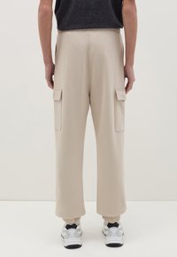 Beige Cargo-Hosen mit zwei Seitentaschen, elastischem Bund und knöchelfreiem Abschluss, aus weichem Material, kombiniert mit weißen und schwarzen Sneakers.