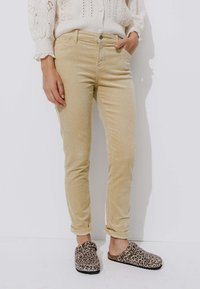 Pantalons en velours côtelé beige à coupe slim, avec une poche avant et des ourlets retroussés, associés à des chaussures à enfiler imprimé léopard.