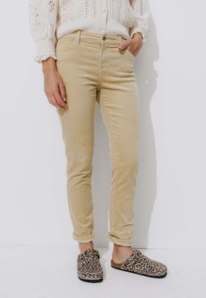 Pantalons en velours côtelé beige à coupe slim, avec une poche avant et des ourlets retroussés, associés à des chaussures à enfiler imprimé léopard.