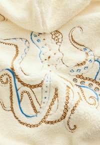 Vilnas sega ar astoņkāja dizainu. Raksturīga krēmkrāsas, zilas un brūnas izšuvums, mīksta tekstūra un izsmalcinātas detaļas.