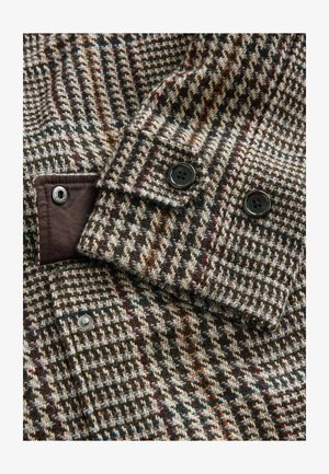 Aitu jaka ar brūnu un krēmīgu šaha rakstu. Iezīmējas ar melniem pogām un kontrastējošu brūnu audumu pie aproces un iekšējā klipa.