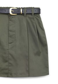 Gonna verde olivo con pieghe e tasche laterali, abbinata a una cintura nera con fibbia dorata.