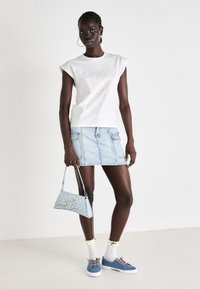 Hvid kortærmet t-shirt med præget tekst, lys blå denim mini nederdel, blå sneakers, mønstret taske og hvide sokker med flæser.