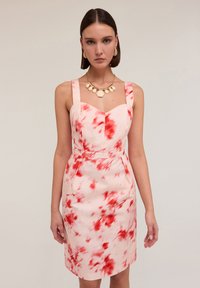 Tajt klänning i mjukt tyg, med en rosa botten och röda blommönster, breda loopar och en hjärtformad halsringning.