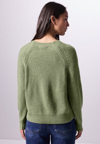 Pullover verde a maglia con texture a coste, scollo rotondo e spalle scese. Rifinito con orlo e polsini a coste.